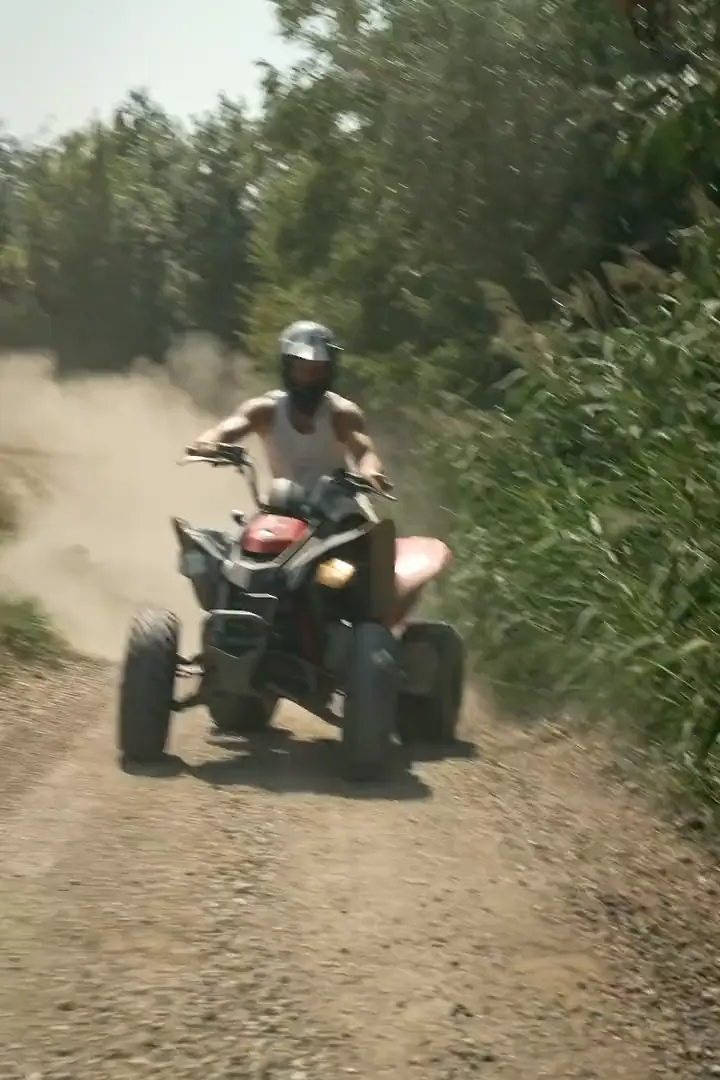 Quad kommt einen Waldweg herunter und zieht eine Staubwolke hinter sich her
